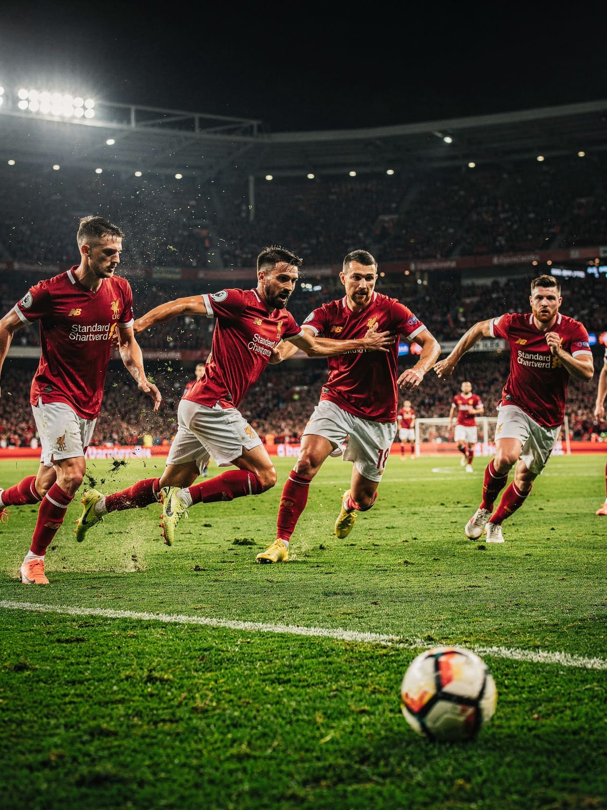 football players in red jerseys competing on pitch under stadium lights