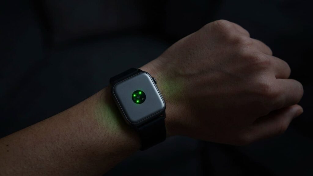 modern smartwatch on wrist showing heart rate sensor glowing green in dim light