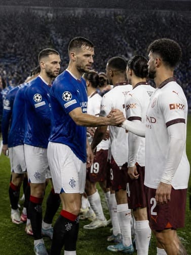 two_football_teams_shaking_hands_on_a_rainy_pitch_with_fans